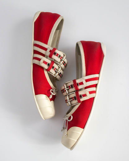 Red sneakers with white stripes and gold buckles on a light gray background