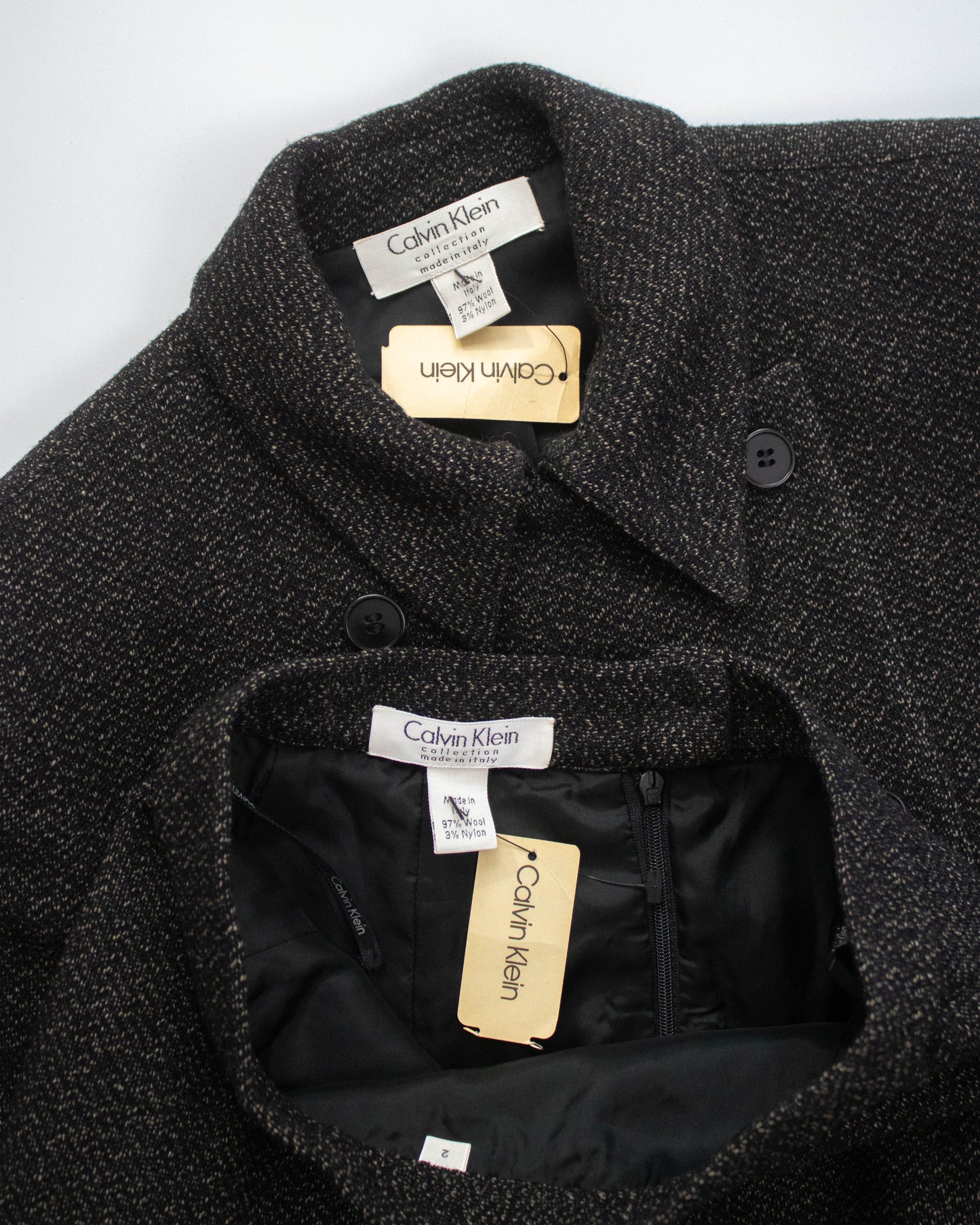 Close-up of a dark textured coat with brand labels on a white background