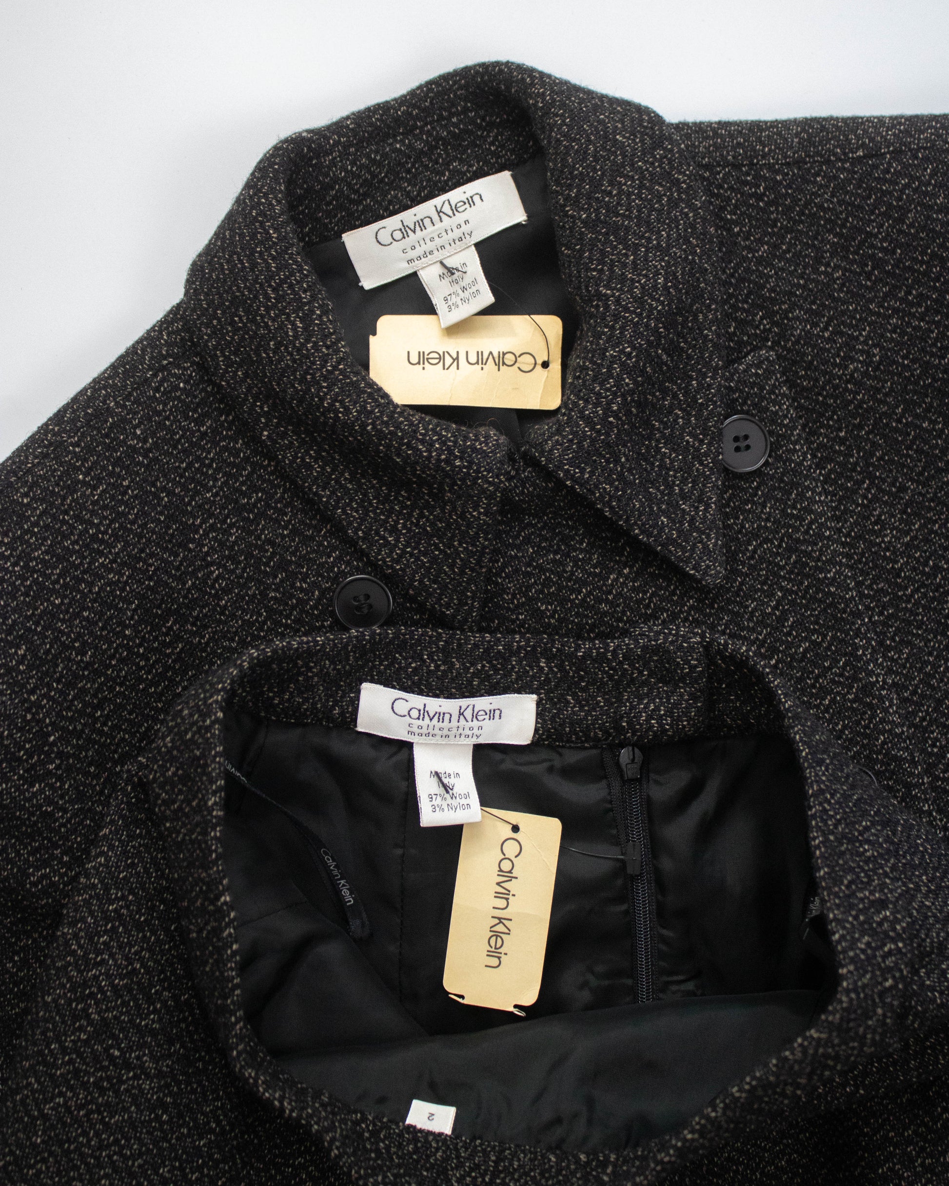 Close-up of a dark textured coat with brand labels on a white background