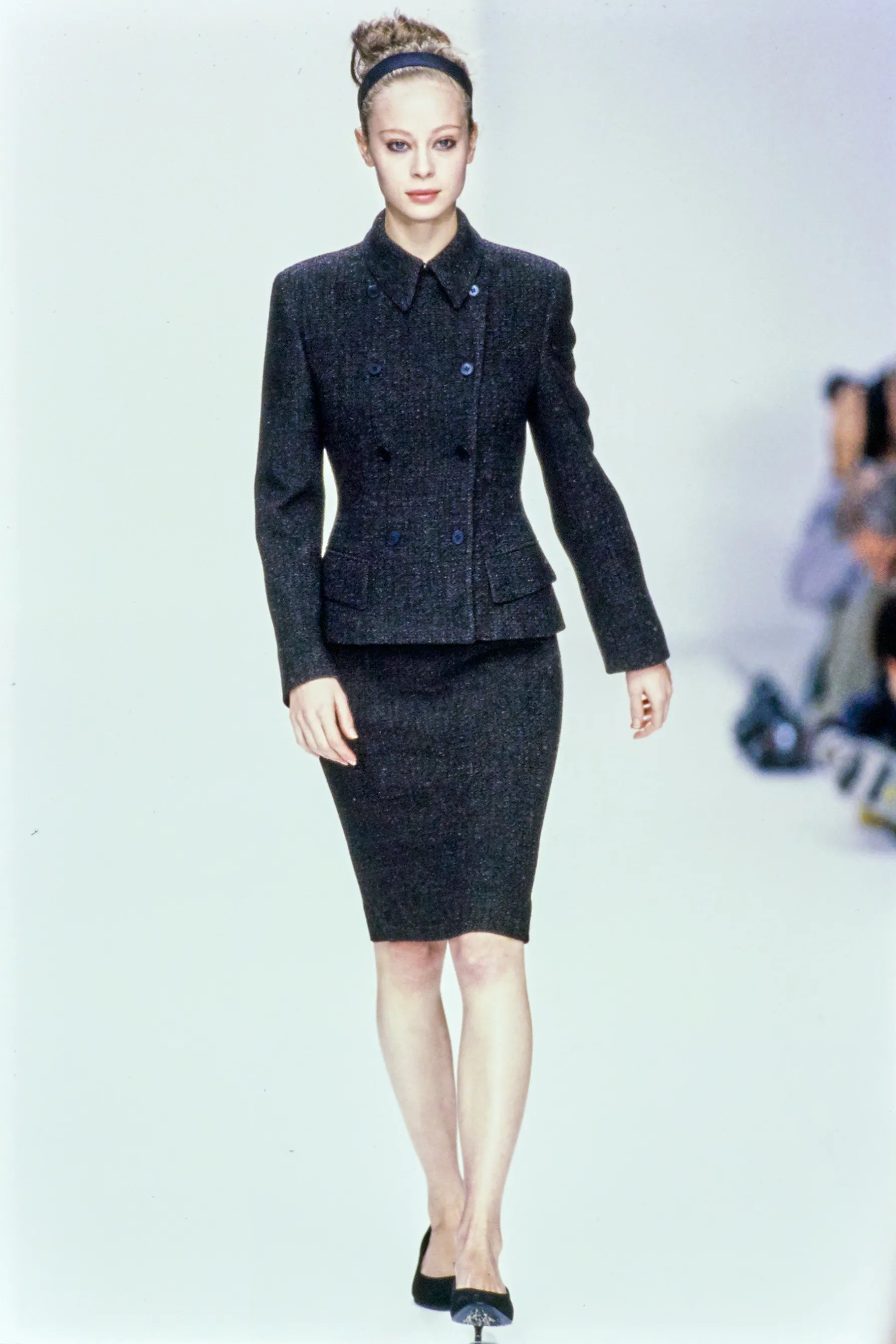 Model wearing a dark gray suit on a runway with a blurred background