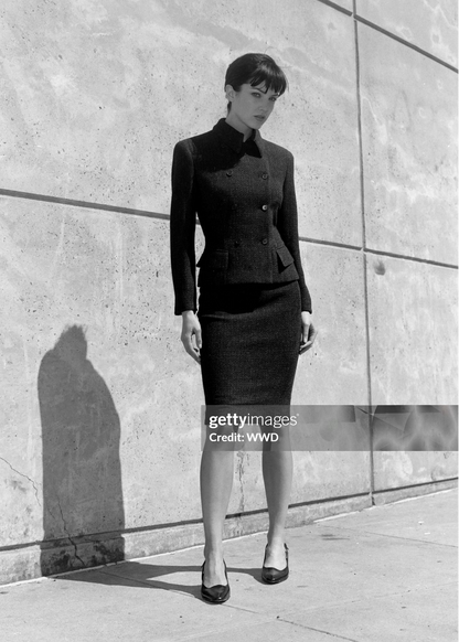 Black and white photo of a woman in a suit standing against a concrete wall.