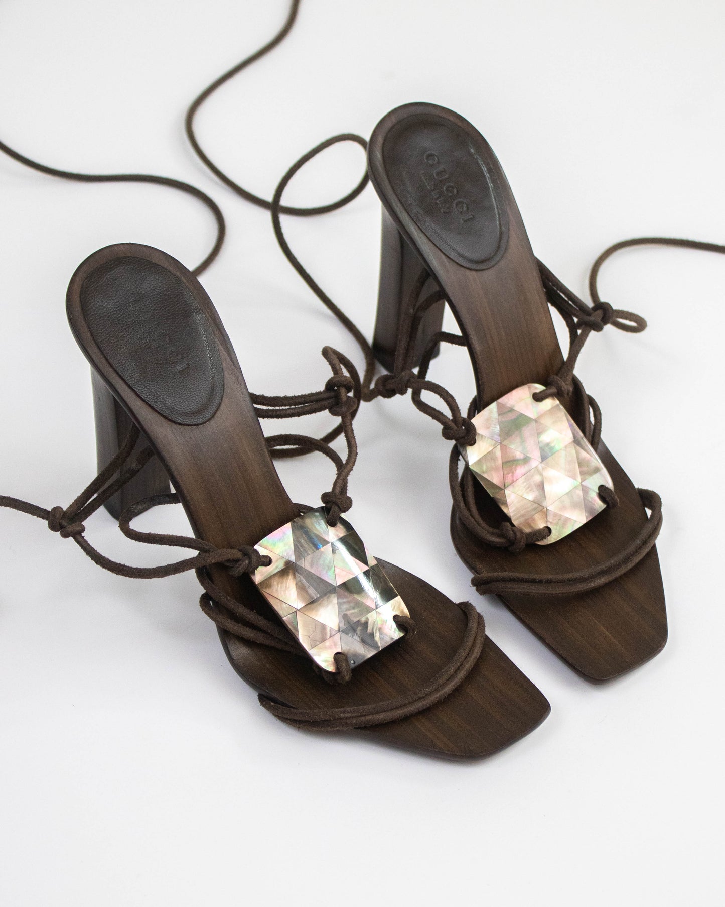A pair of dark brown block-heel mule sandals with lace-up front straps and large iridescent rectangular rhinestone embellishments, shown on a plain white background.