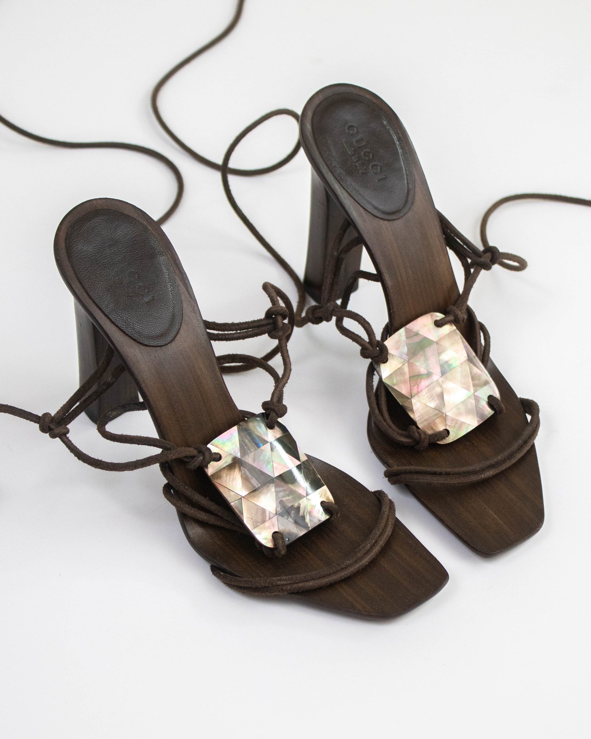 A pair of dark brown block-heel mule sandals with lace-up front straps and large iridescent rectangular rhinestone embellishments, shown on a plain white background.