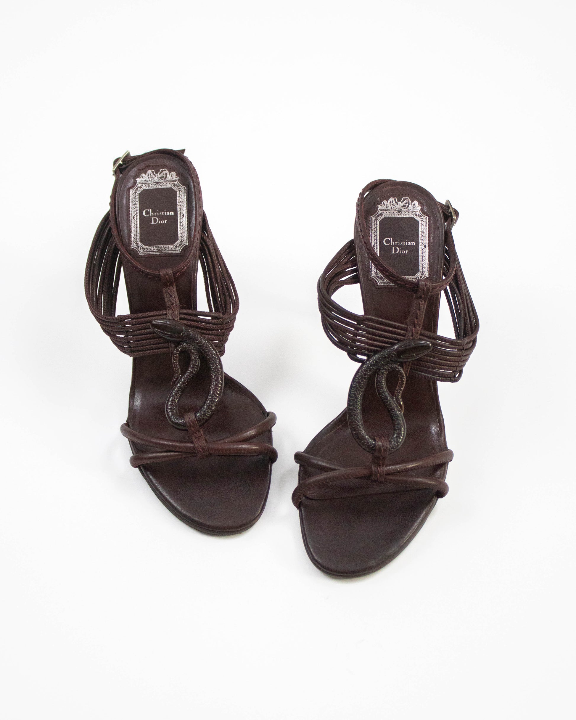 Pair of brown high-heeled sandals with 'Christian Dior' logo on a white background