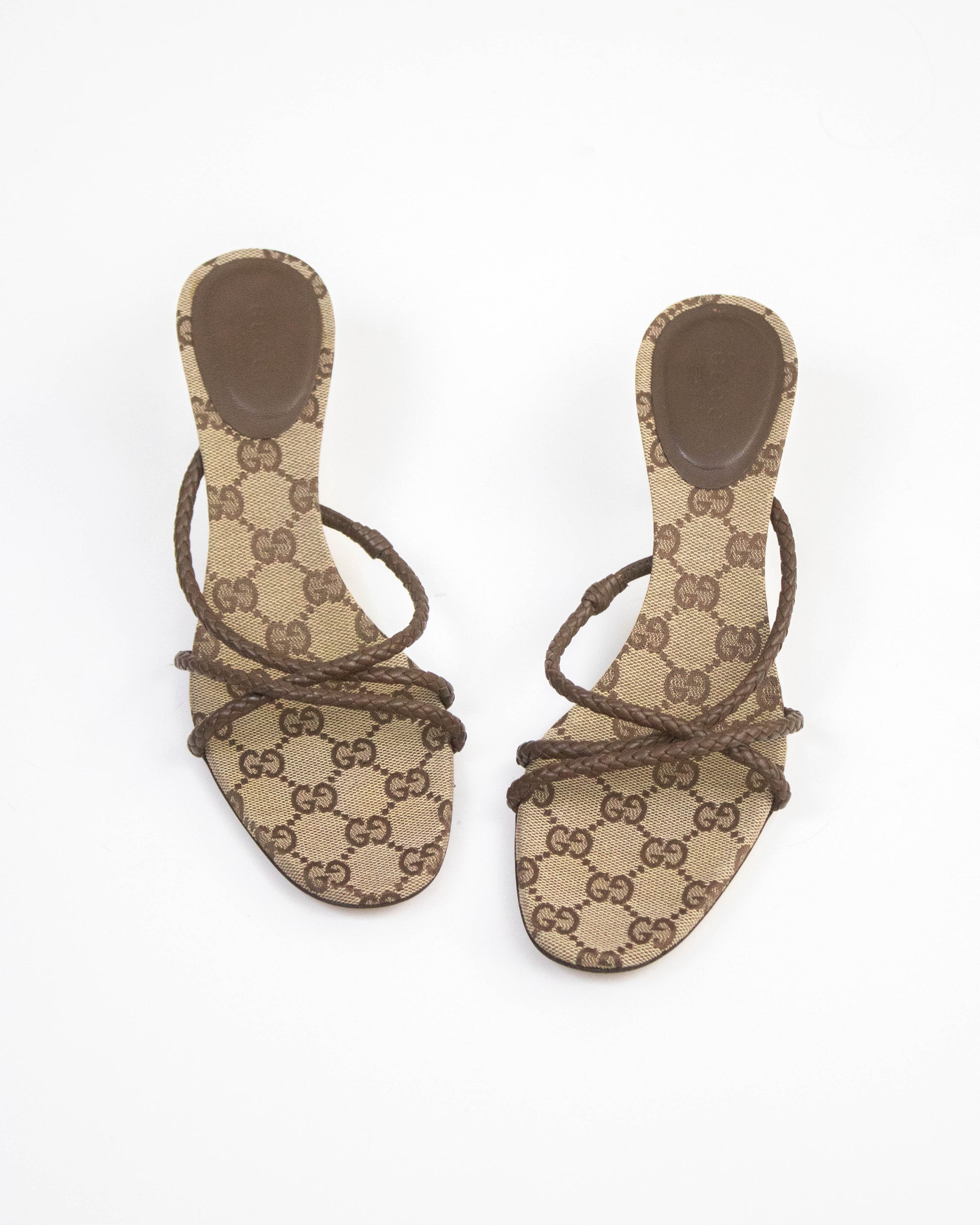 A pair of Gucci flat slide sandals featuring the brand's signature brown and beige GG monogram canvas, with brown leather straps wrapped around the toes, shown against a plain white background.