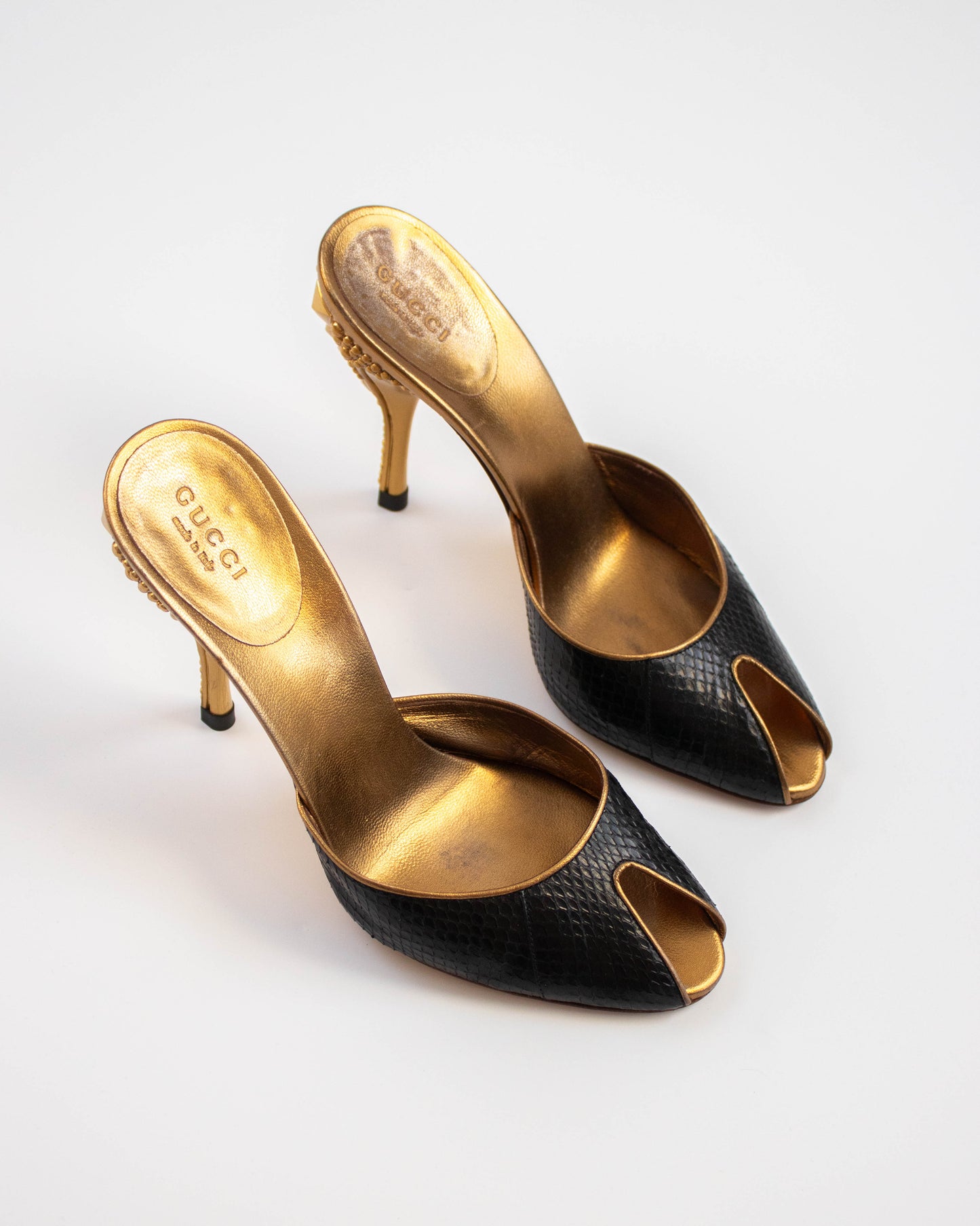 Black and gold high-heeled shoes with 'Gucci' branding side view