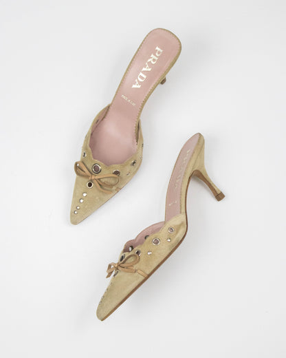 Pair of beige high-heeled shoes with decorative elements on a light gray background