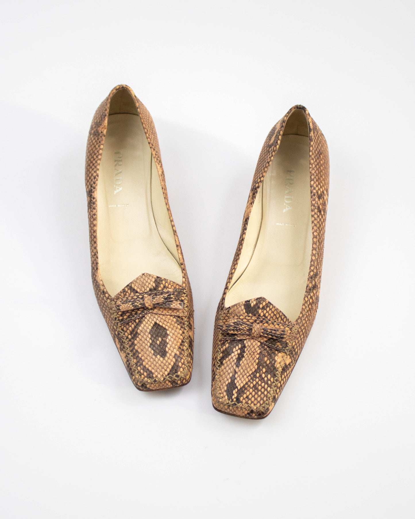 Pair of brown snake print Prada heels on a white background