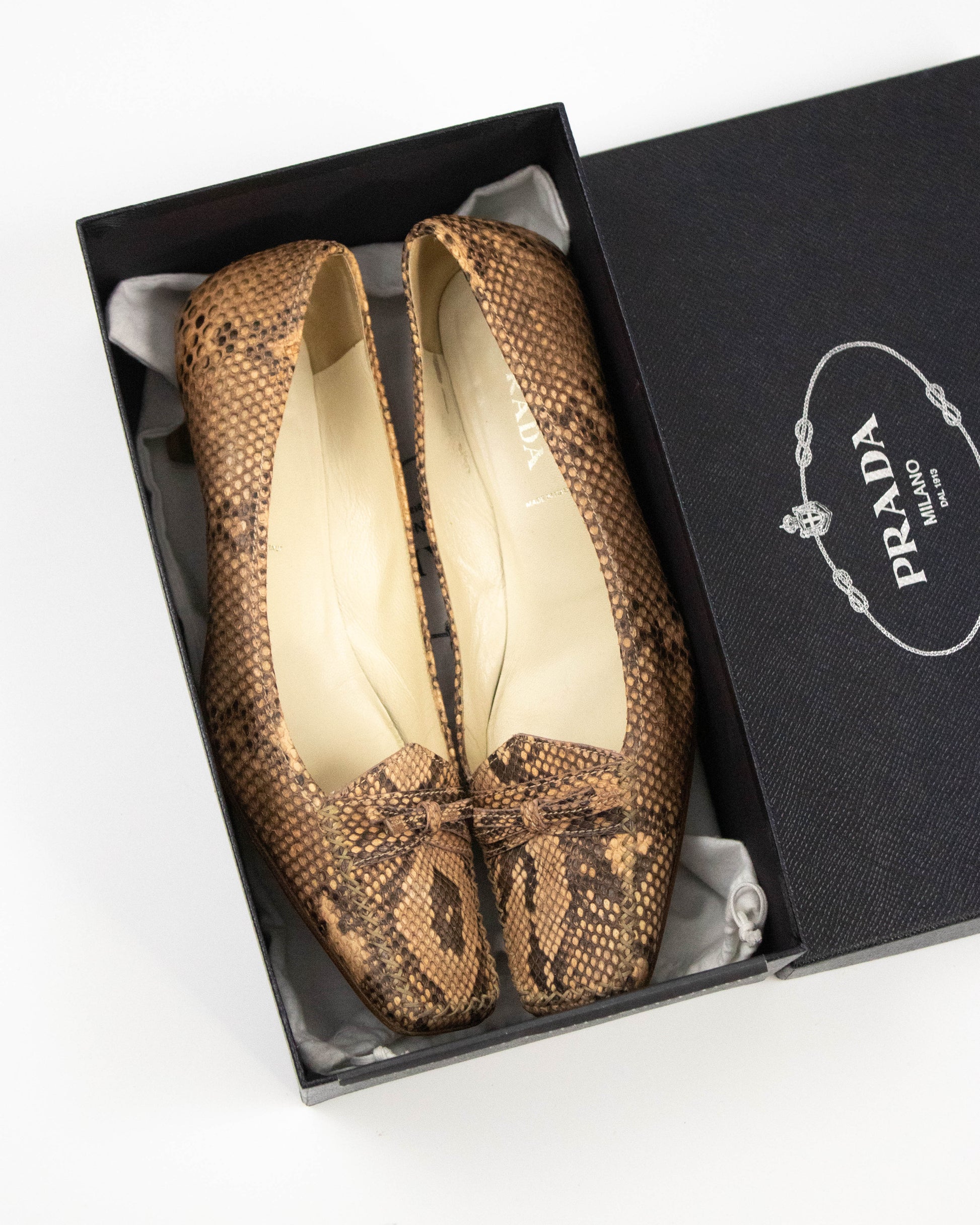 Pair of brown snake print Prada heels on a white background