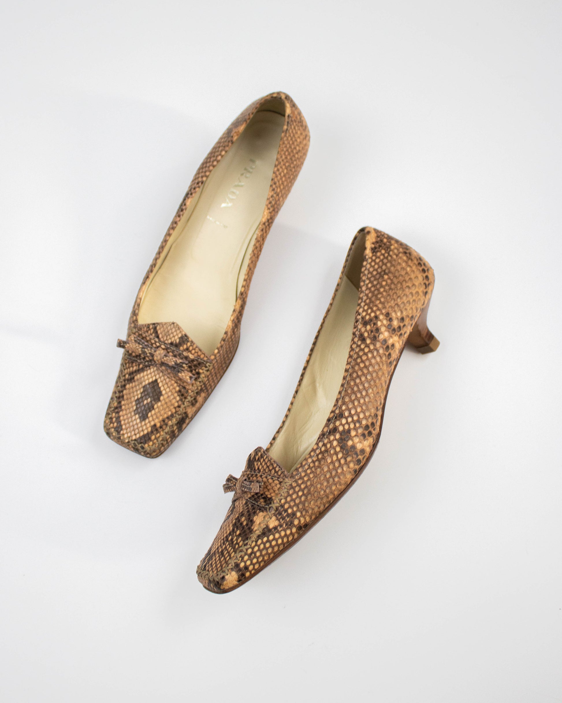Pair of brown snake print Prada heels on a white background