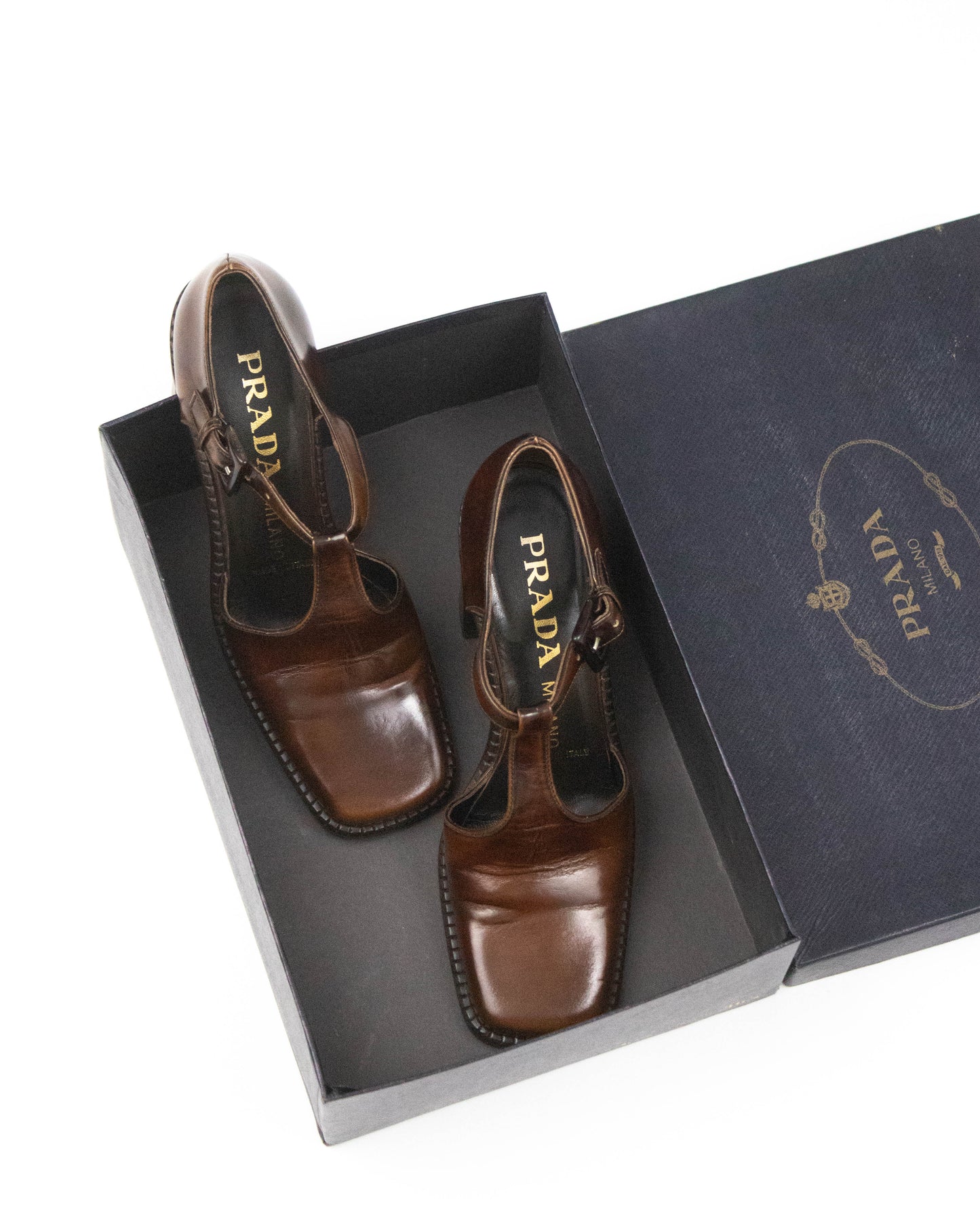 Brown Prada sandals in an open Prada box on a white background