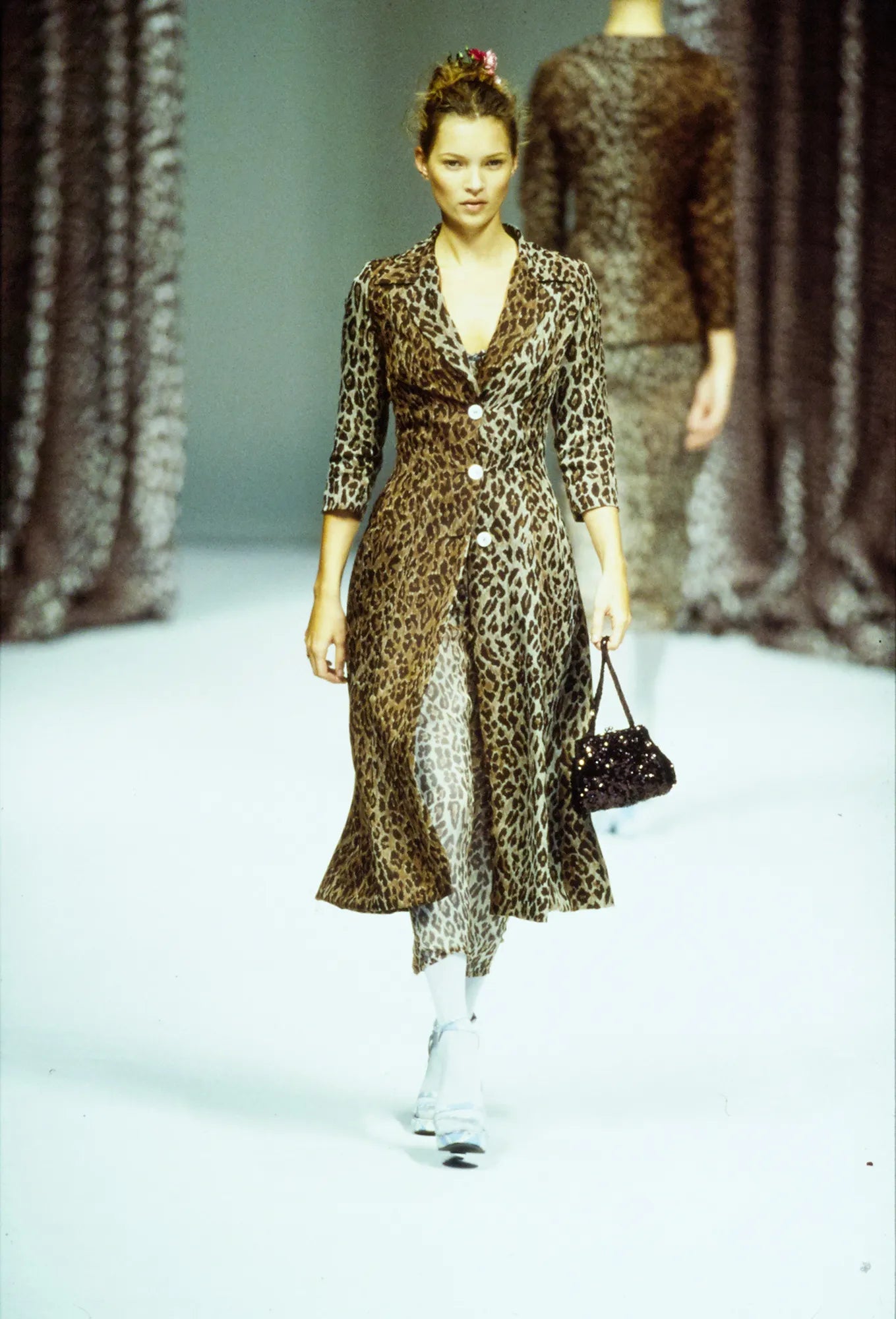 Model walking on a runway wearing a leopard print dress with a blurred background