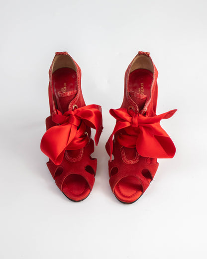 Pair of red high-heeled shoes with large bows on a white background